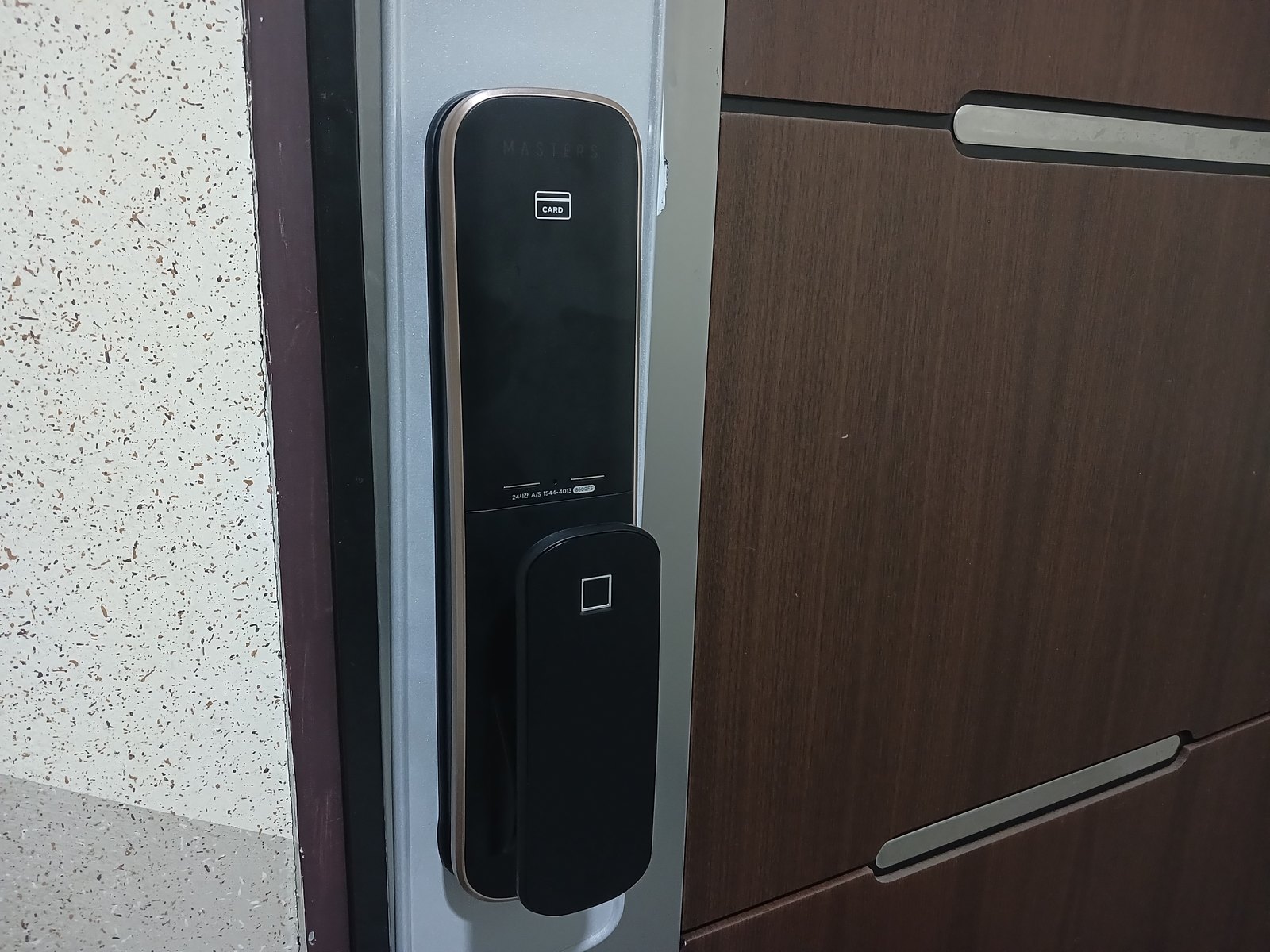 강북구 미아동 출장 — 짙은 갈색 문 가장자리 은회색 긴 판에 달린 검은 푸시풀 도어락, 구리빛 테와 카드 표시